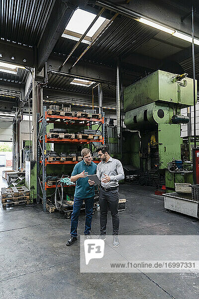Male colleagues using digital tablet while standing manufacturing factory