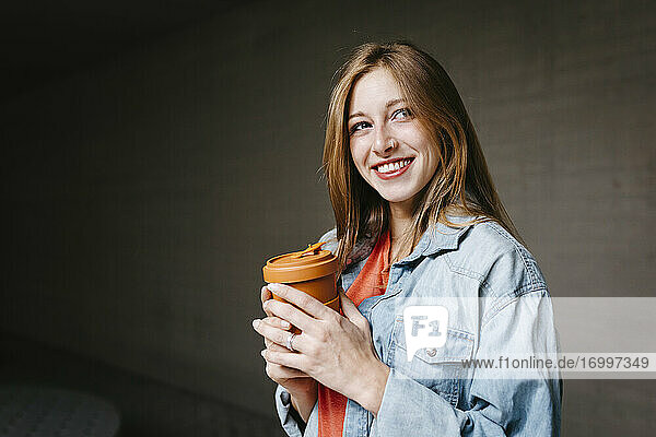 Glückliche schöne junge Frau mit wiederverwendbarem Kaffeebecher auf dem Universitätscampus