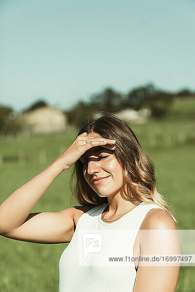 Junge Frau  die im Sommer im Park ihre Augen mit der Hand abschirmt