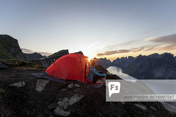 Woman sitting in camp on mountain during sunset at Reinebringen. Lofoten  Norway