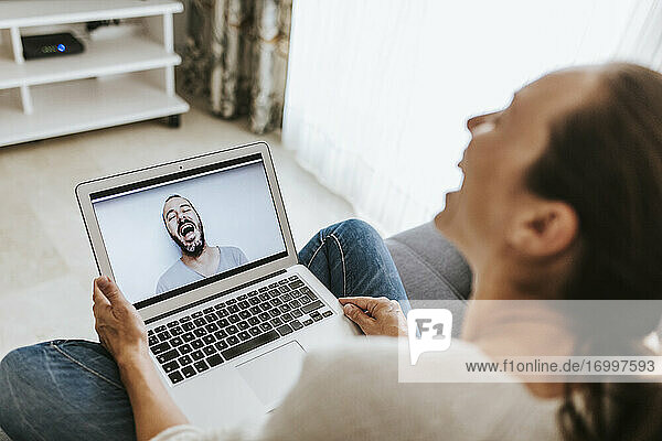 Frau und Mann lachen bei einem Videoanruf im heimischen Wohnzimmer