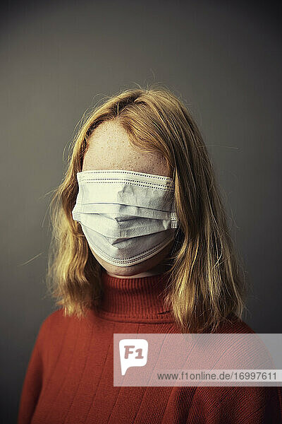 Teenager-Mädchen  das sein ganzes Gesicht mit einer Schutzmaske bedeckt  während es vor einem grauen Hintergrund steht