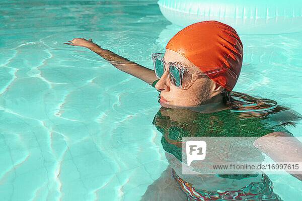 Porträt einer Frau im Schwimmbad mit roter Badekappe  grünem Strickpullover und verspiegelter Sonnenbrille