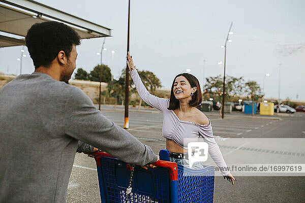 Carefree woman sitting in shopping cart by man