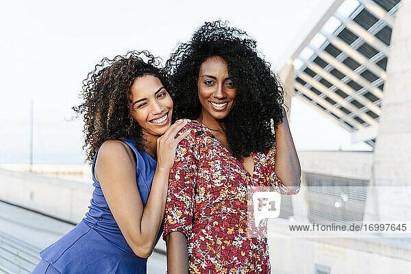 Lächelnde junge Freundinnen in Freizeitkleidung auf dem Dach stehend