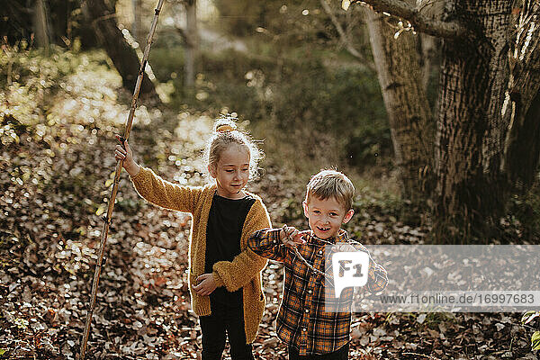 Girl and boy playing with stick and rope while standing in forest during autumn
