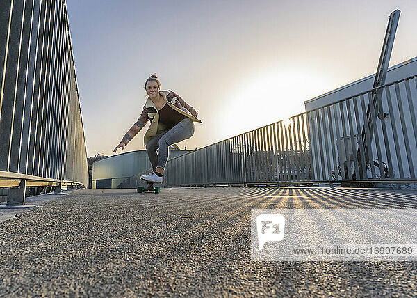 Glückliche Frau auf dem Skateboard gegen den klaren Himmel bei Sonnenuntergang