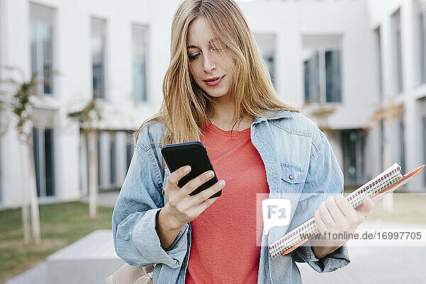 Junge blonde Studentin mit Smartphone an der Universität