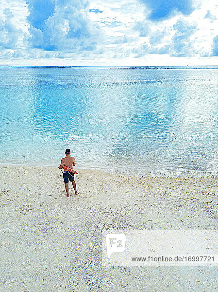 Männlicher Tourist mit aufblasbarem Ring  der am Ufer steht und das Meer gegen den Himmel betrachtet