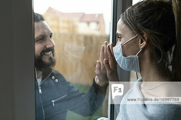 Couple touching hands from window glass during COVID-19 outbreak