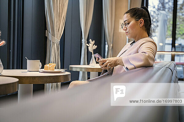 Geschäftsfrau  die ein Mobiltelefon benutzt  während sie in einem modernen Cafe sitzt