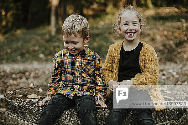 Lächelnde Schwester sitzt bei ihrem Bruder im Wald im Herbst