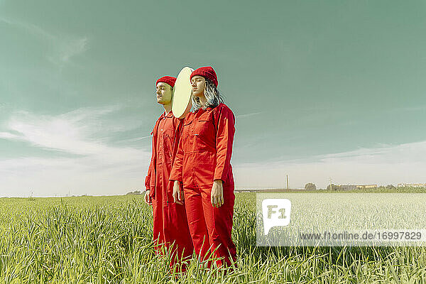 Junges Paar in roten Overalls steht auf einem Feld mit grünem Kreis