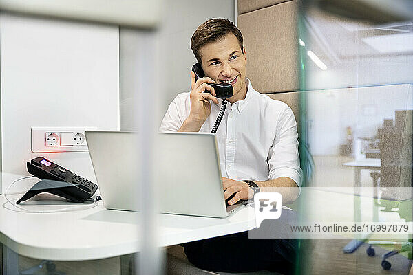 Geschäftsmann lächelnd beim Telefonieren im Büro sitzend