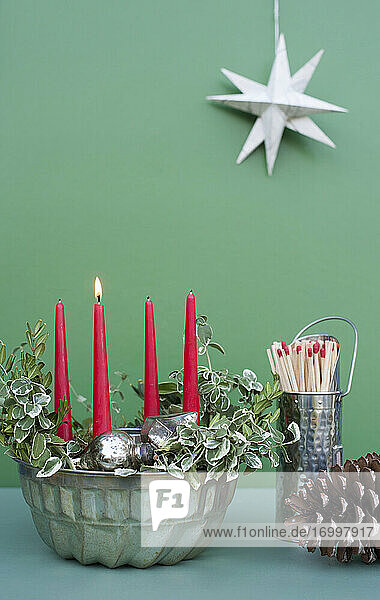 Studioaufnahme von selbst gebastelter Adventsdekoration mit Kerzen  Zweigen  Tannenzapfen  Streichhölzern und Backform