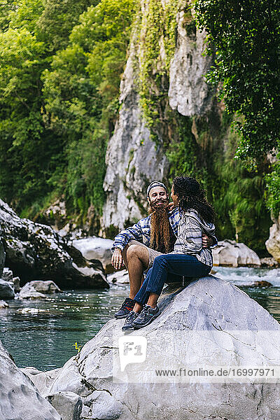 Happy young couple sitting on rock while hiking in Picos De Europa mountain  Asturias  Spain