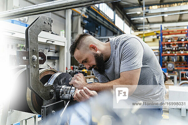 Professional male engineer fastening nut on machine in illuminated industry
