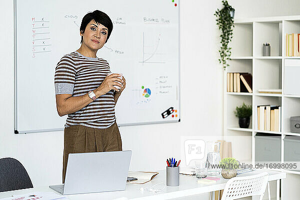 Portrait of businesswoman posing in office with mug in hands