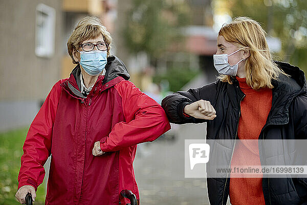 Enkelin und Mutter mit Gesichtsmaske grüßen mit Ellbogenstoß  während sie im Freien stehen