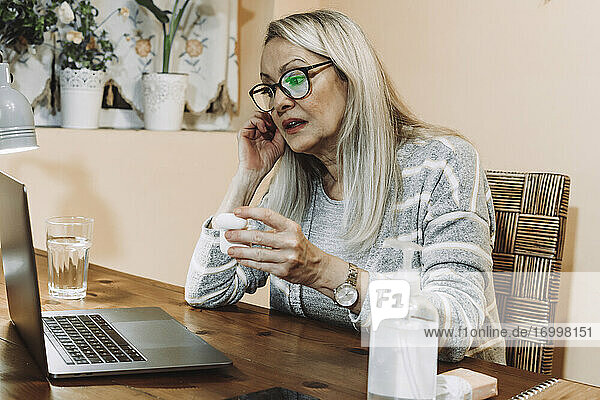 Senior woman wearing wireless in-ear headphones during online consultation at home