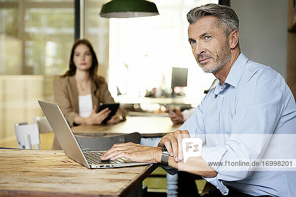 Älterer Geschäftsmann  der wegschaut  während er mit Kollegen im Hintergrund im Büro sitzt