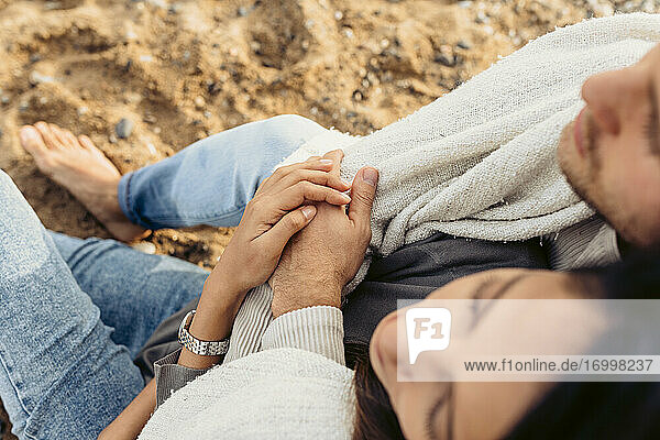 Junge Frau und Freund umarmen sich  während sie am Strand sitzen