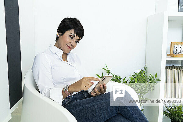 Porträt einer Geschäftsfrau  die in einem Bürosessel sitzt und ihr Smartphone in den Händen hält