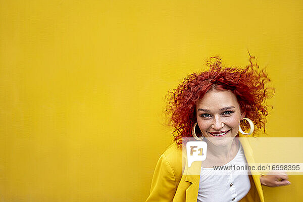 Glückliche junge Frau mit roten lockigen Haaren vor gelber Wand