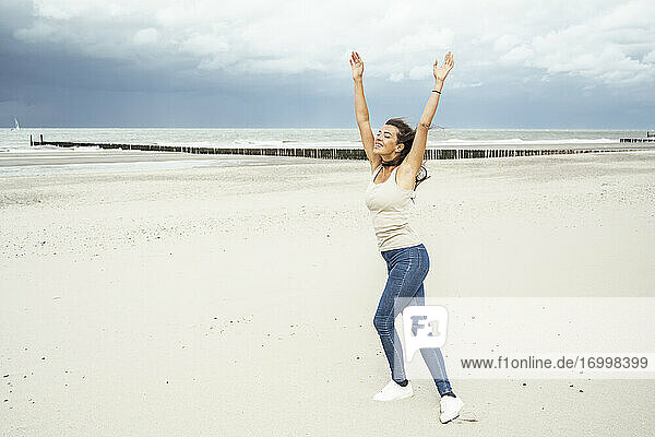 Junge Frau mit erhobenen Armen beim Tanzen am Strand