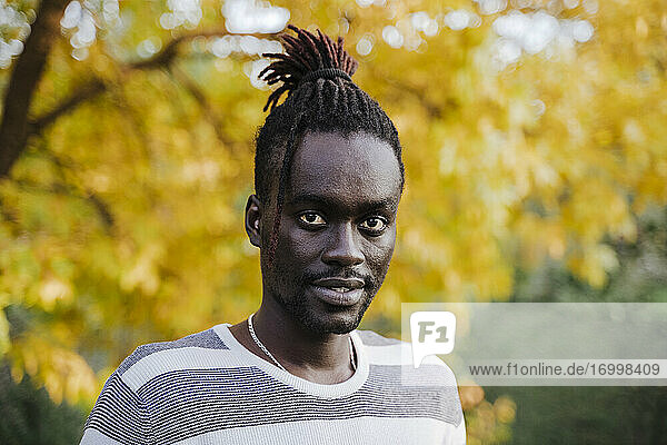 Afrikanischer Mann  der im Herbst gegen einen gelben Baum im Park steht