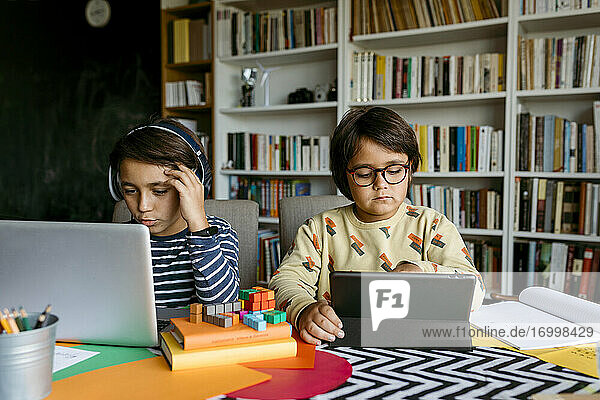 Junge beim E-Learning mit Laptop  während sein Freund am Tisch mit einem digitalen Tablet lernt