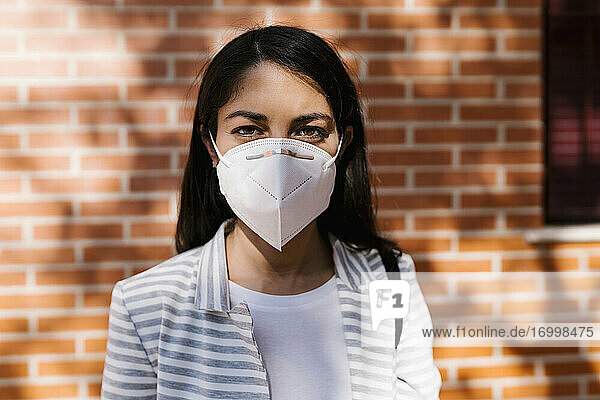 Selbstbewusste Frau mit Gesichtsschutzmaske vor einer Mauer während COVID-19