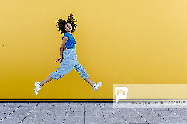 Hübsche Frau springt vor Freude vor einer gelben Wand