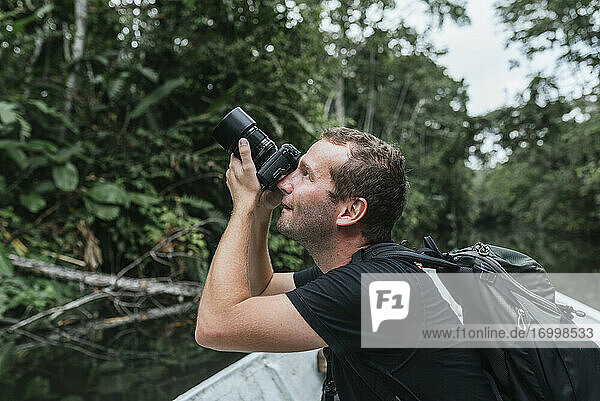 Male backpacker photographing nature from canoe at Napo River  Ecuador