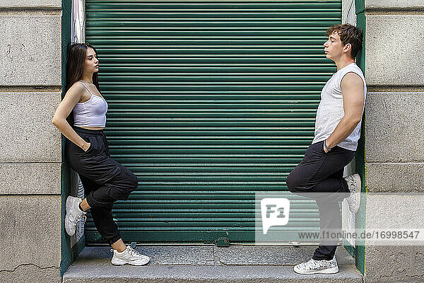 Young man and woman leaning on wall against shutter