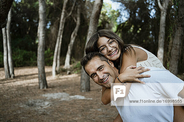 Happy father giving piggyback to daughter in forest