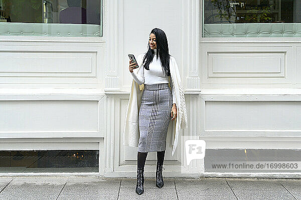 Fashionable businesswoman using mobile phone against wall