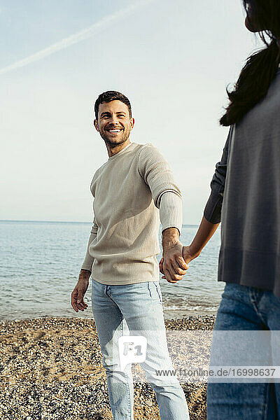 Lächelnder Mann  der die Hand einer Frau hält  während er am Strand steht