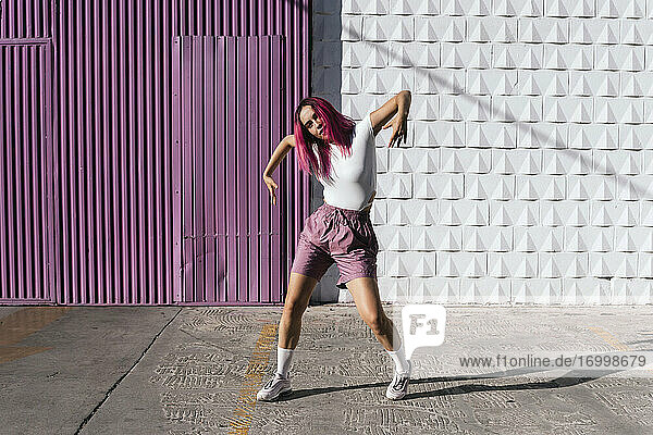 Junge Frau mit gefärbten roten Haaren tanzt vor einer lila Wand in der Stadt