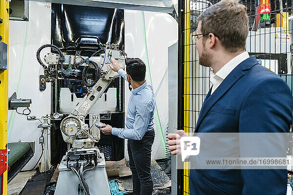 Coworkers looking at robotic arm while standing in factory