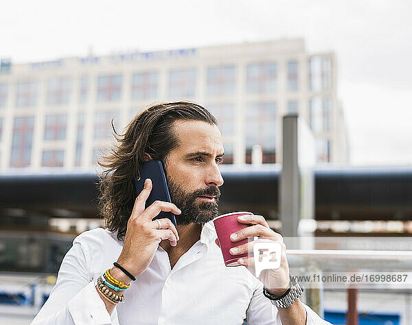 Candid portrait of bearded businessman sitting outdoors and talking on smart phone