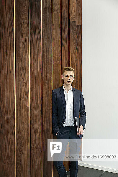 Confident entrepreneur holding digital tablet leaning on wooden wall