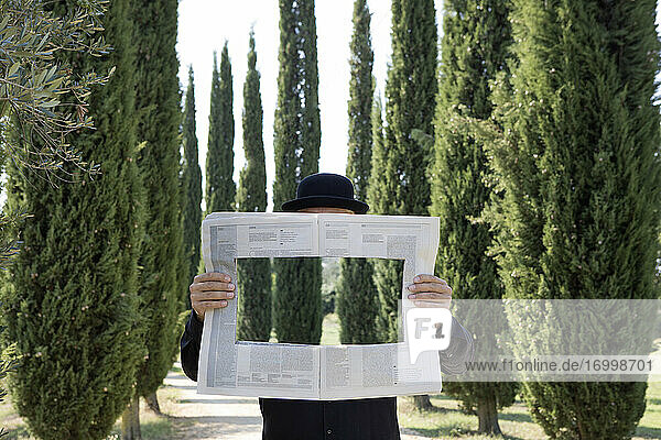 Italy  Tuscany  invisible man surrounded by cypresses reading newspaper with a hole
