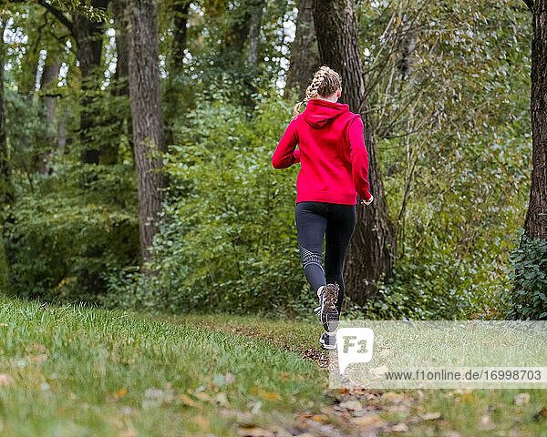Young sportswoman jogging on grass in forest