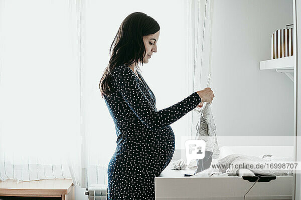 Schwangere Frau betrachtet Babykleidung zu Hause