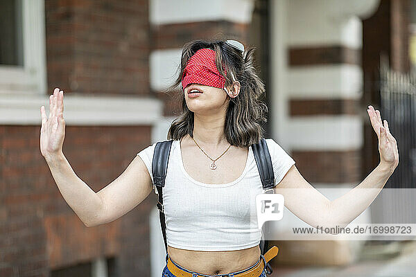Junge Frau mit roter Gesichtsmaske auf dem Auge gestikuliert  während sie in der Stadt steht
