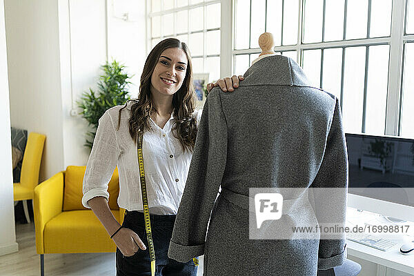 Lächelnde Modedesignerin steht neben einer Schaufensterpuppe im Atelier