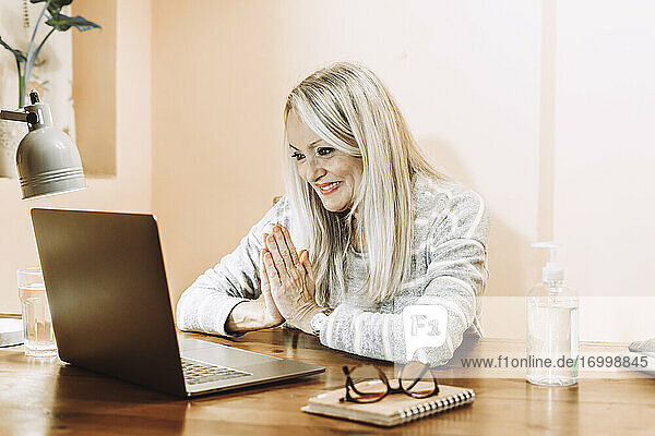 Lächelnde ältere Frau  die während einer medizinischen Online-Konsultation zu Hause grüßt