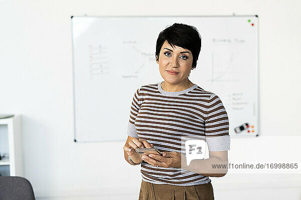 Porträt einer Geschäftsfrau im Büro stehend mit Smartphone in den Händen