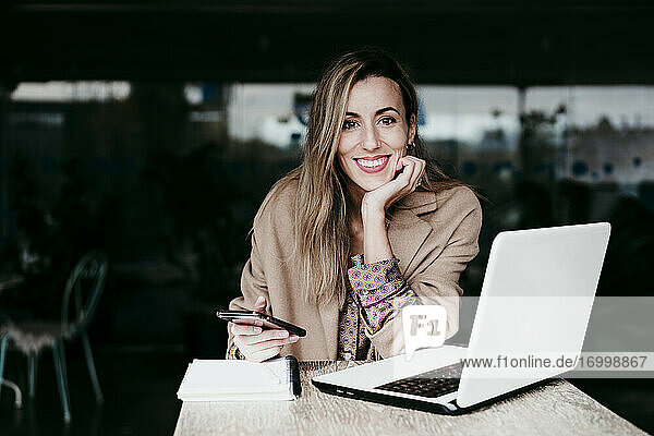 Schöne Geschäftsfrau sitzend mit Hand am Kinn am Schreibtisch arbeiten im Büro